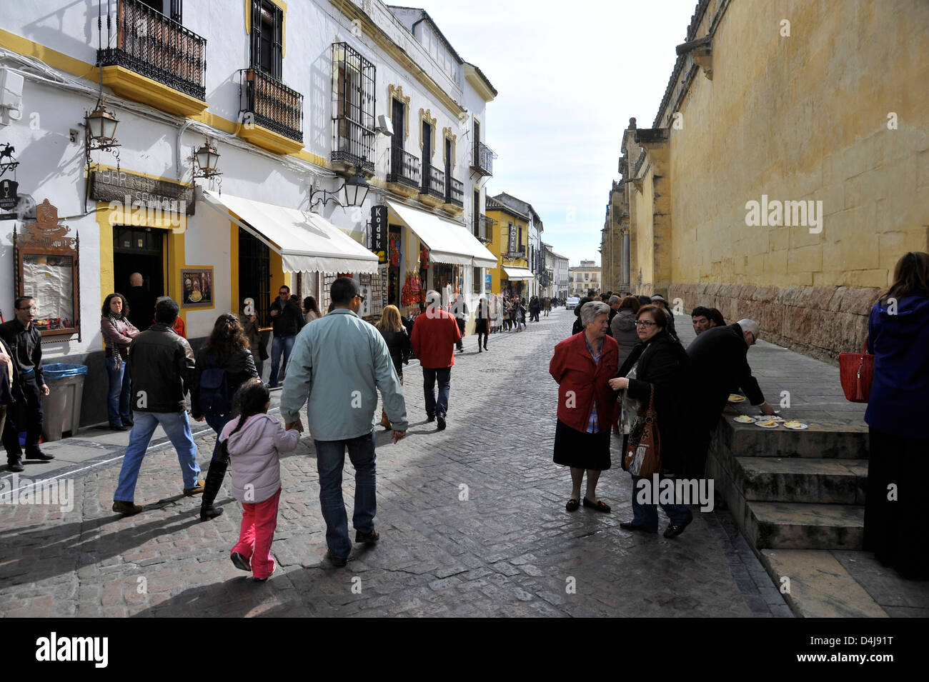 Mid-Day on a Sunday people crowd a street outside the Mezquita Mosque-Cathedral in Cordoba, Andalusia, Spain, and consume drinks Stock Photo