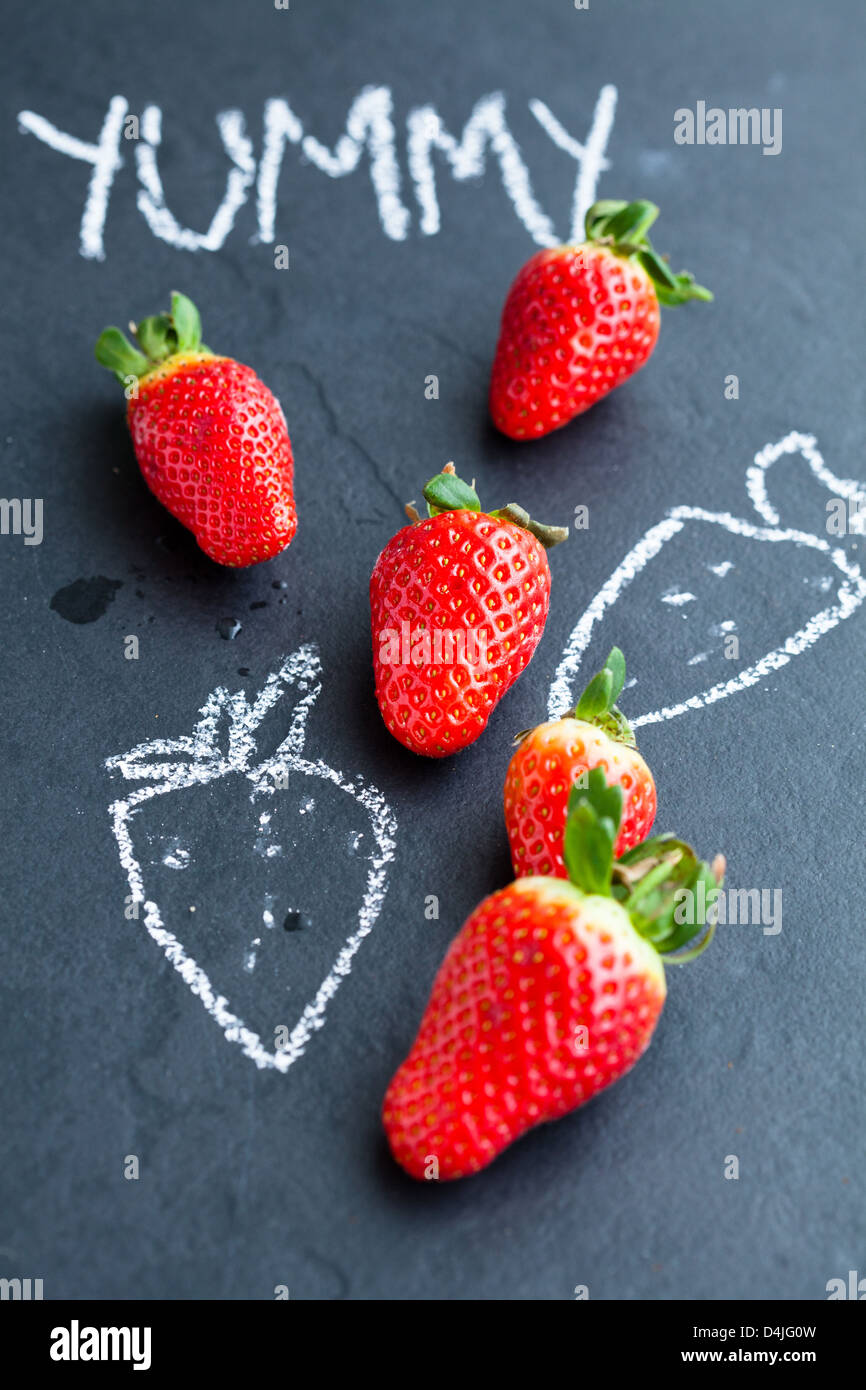 Fresh whole strawberries and chalk drawings and yummy word on dark background Stock Photo