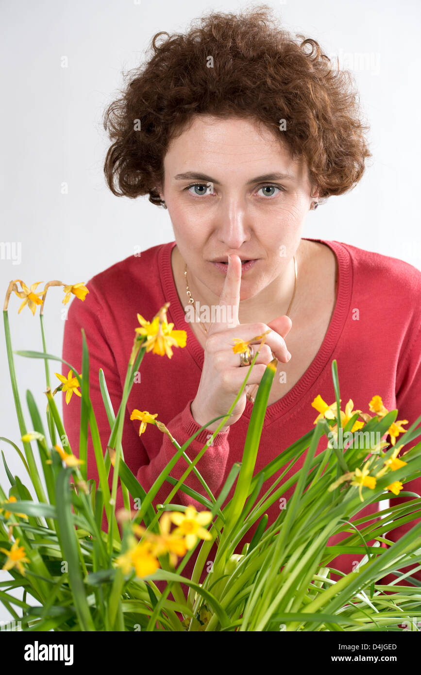 young woman with curly hair and red pullover holding finger in front of her lips Stock Photo