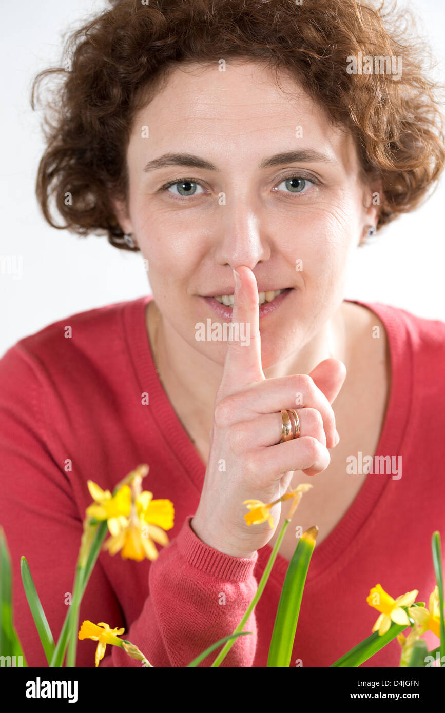 young woman with curly hair and red pullover holding finger in front of her lips Stock Photo