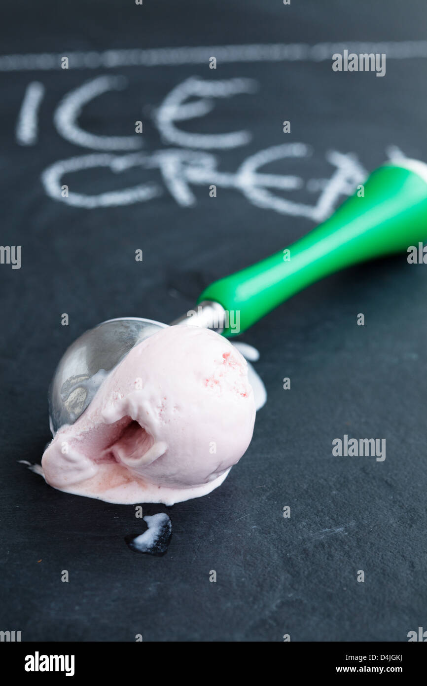 Closeup of strawberry ice cream and scoop on dark background with text written in chalk Stock Photo