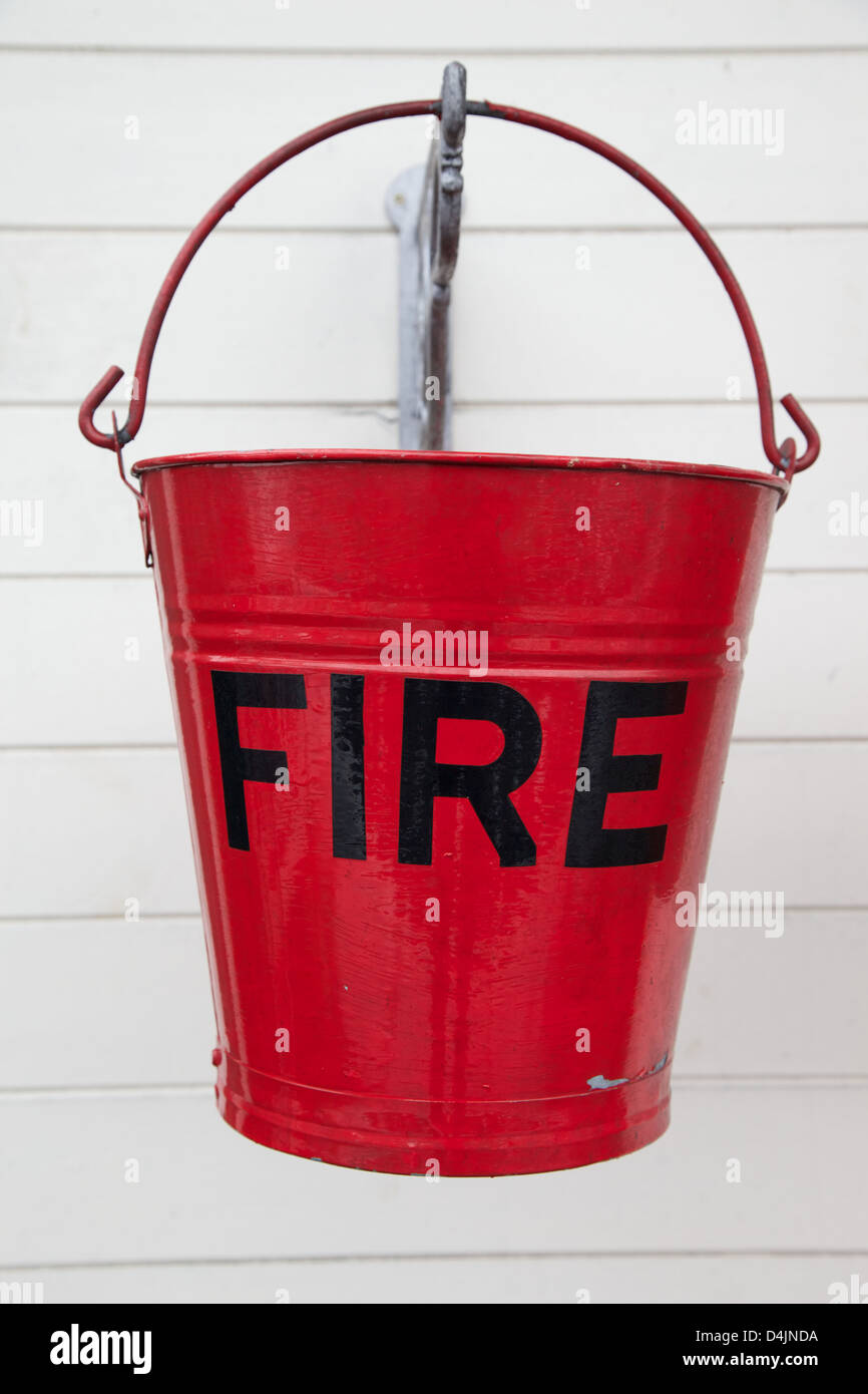 Old metal fire buckets hanging against a whitewashed wooden wall Stock Photo