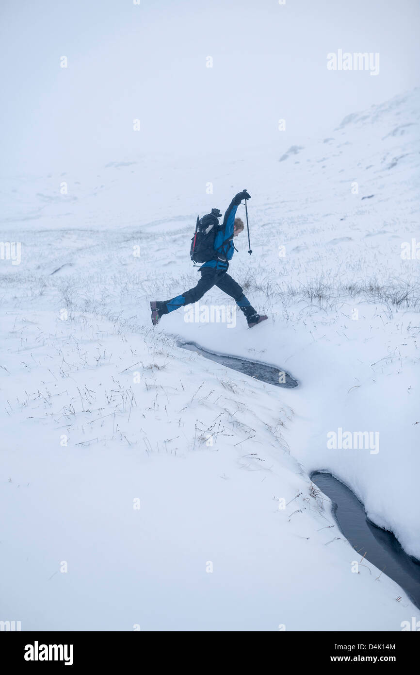 Hiker jumping in snowy landscape Stock Photo