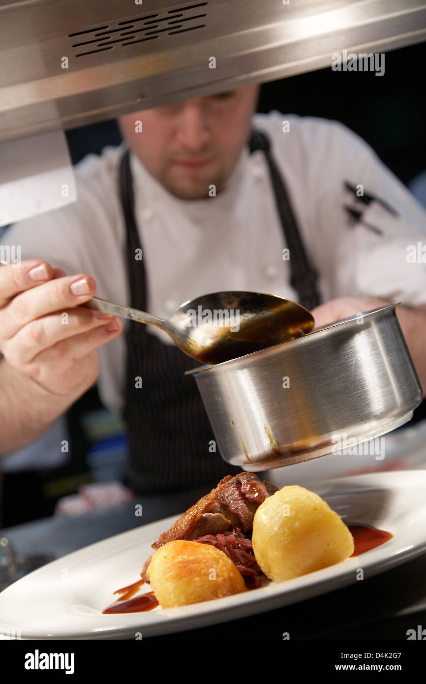Chef drizzling gravy over Roast duck and potatoes in a restaurant in