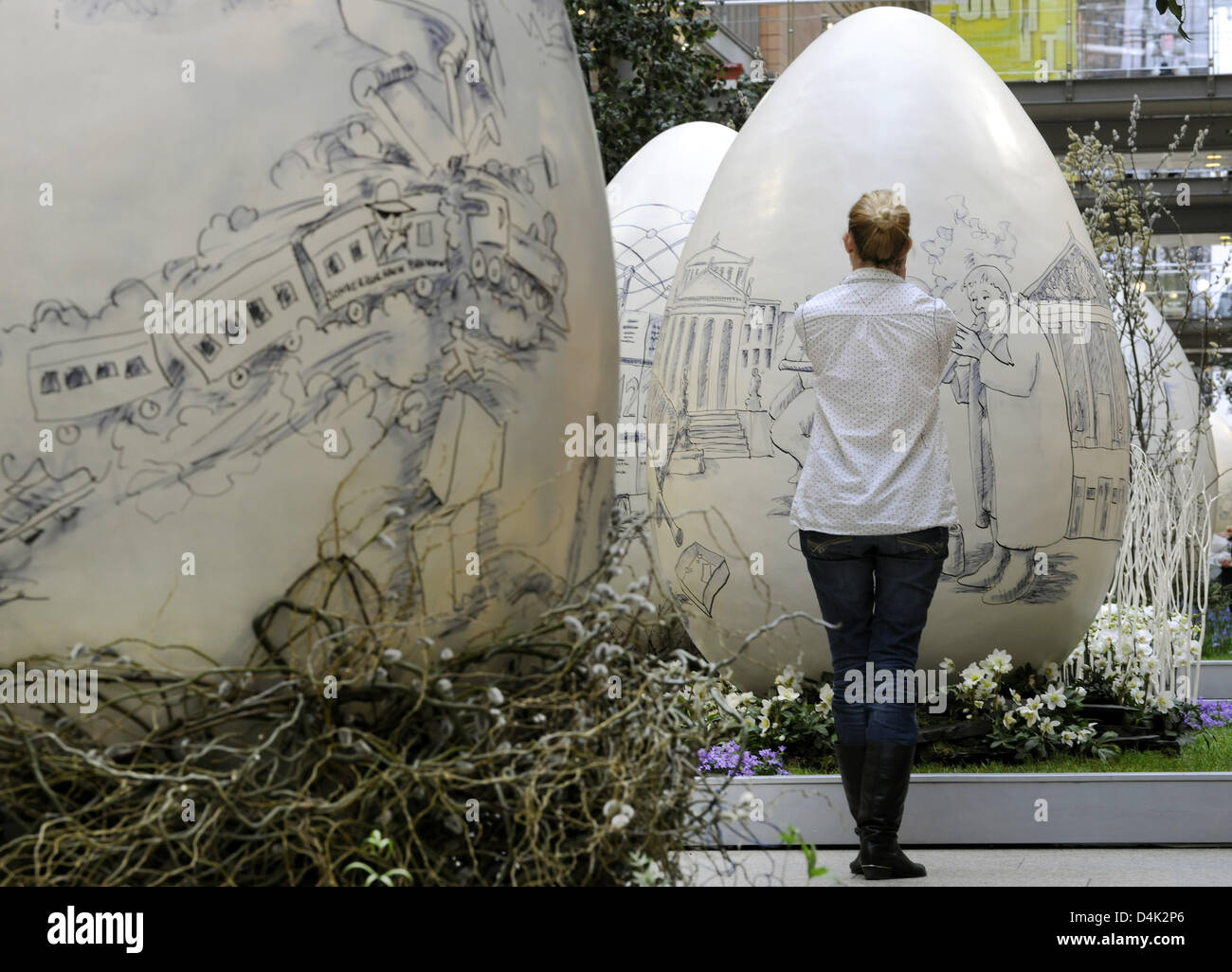 A woman reviews 2,5m high ?Easter Eggs? placed at ?Potsdamer Platz Arcades? as decoration in Berlin, Germany, 23 March 2009. The eggs were designed and painted on with cartoons by artist Knut Weise. Photo: TIM BRAKEMEIER Stock Photo