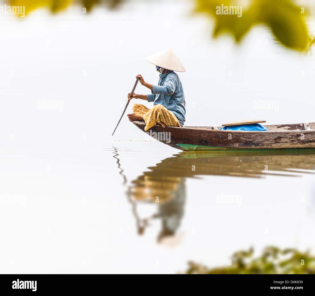 Woman in conical hat sitting on canoe and rowing. Traditional asian boat made of wood. Person holding paddle in hands. Ripple on Stock Photo