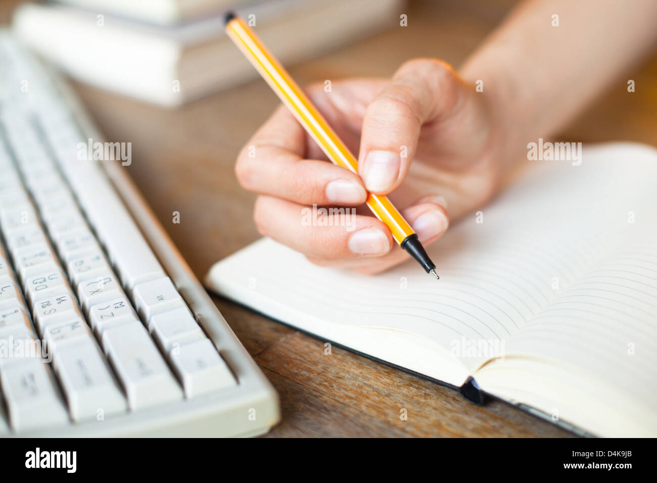 Keyboard Writing Notebook Hands writes in a notebook, keyboard, a stack of books in background ...