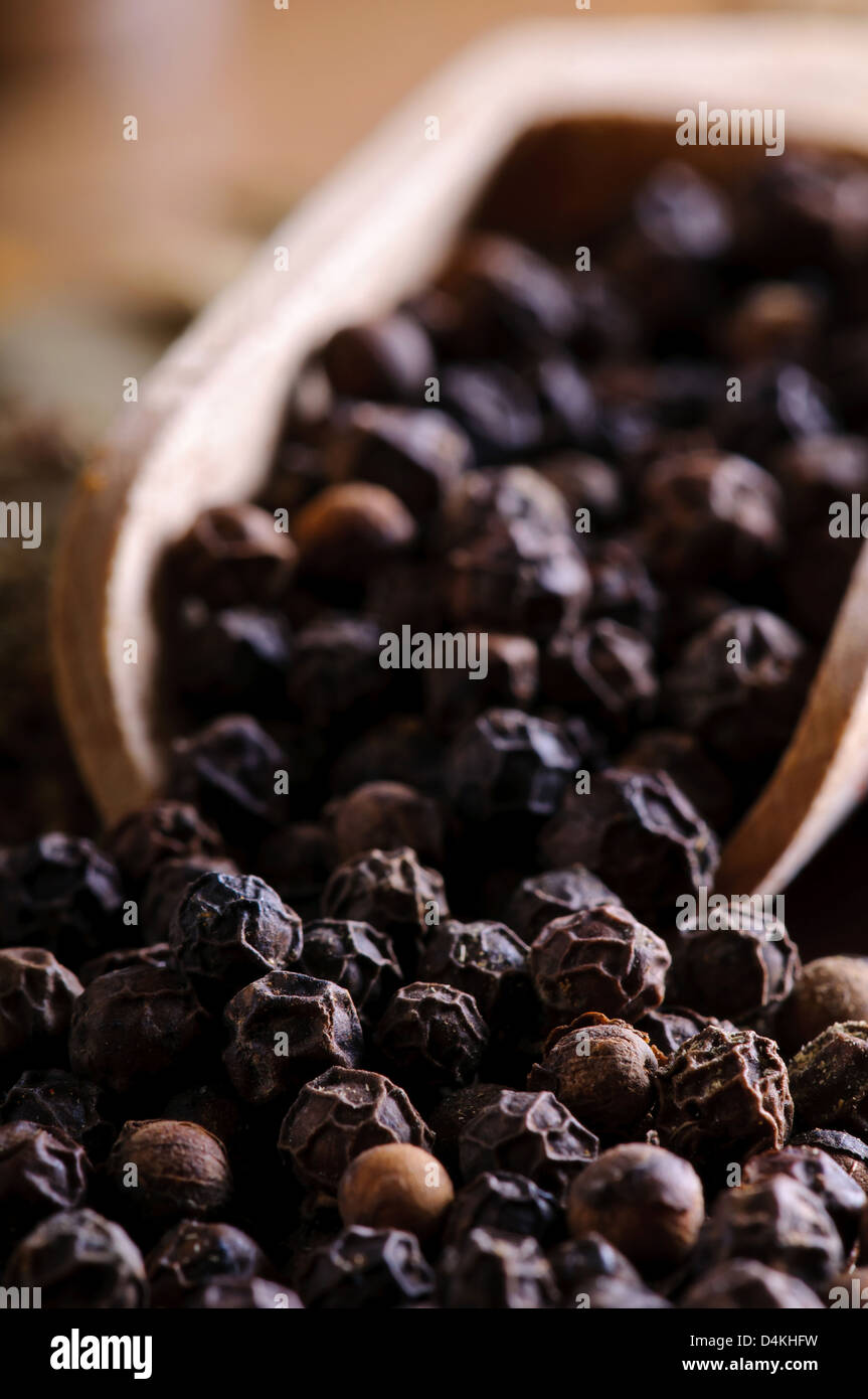 Background with close up of black pepper in a wooden spoon Stock Photo