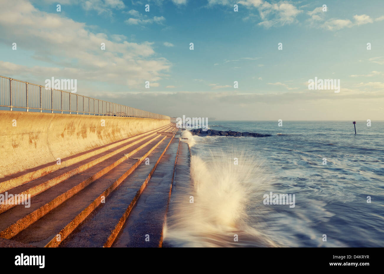 Waves breaking against the sea wall at Southwold, Suffolk in the early morning sunlight Stock Photo