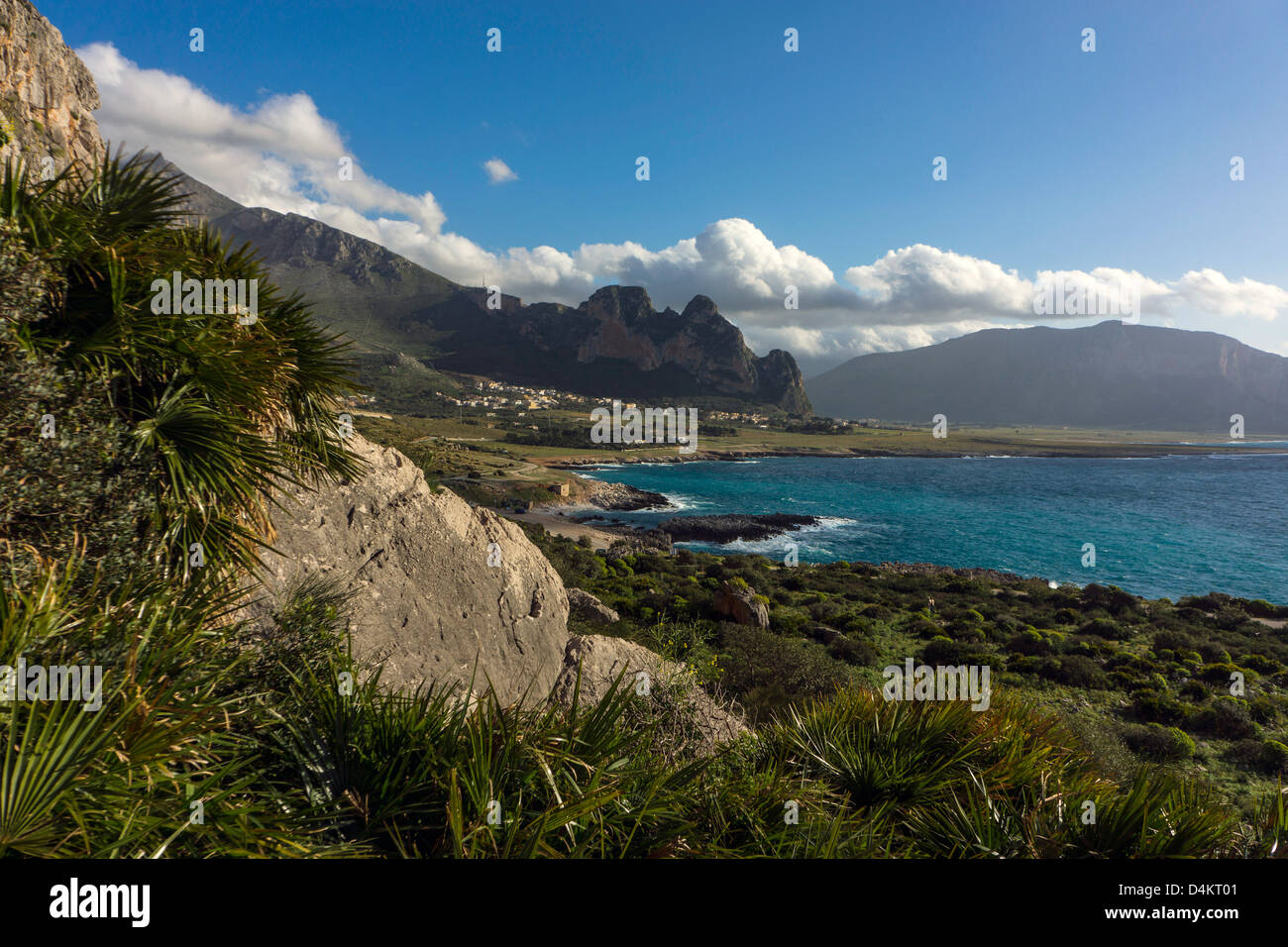 Spring greenery, rocky landscape blue sea and distant mountains, cumulus clouds, San Vito lo Capo, Sicily Stock Photo
