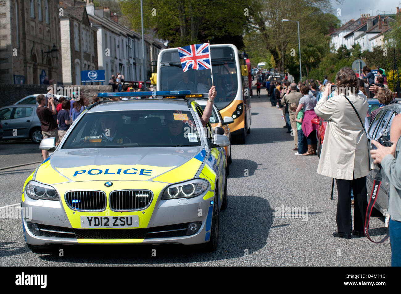 Police wave union jack flag out car window. People of falmouth line the streets to see the olympic torch runners Stock Photo