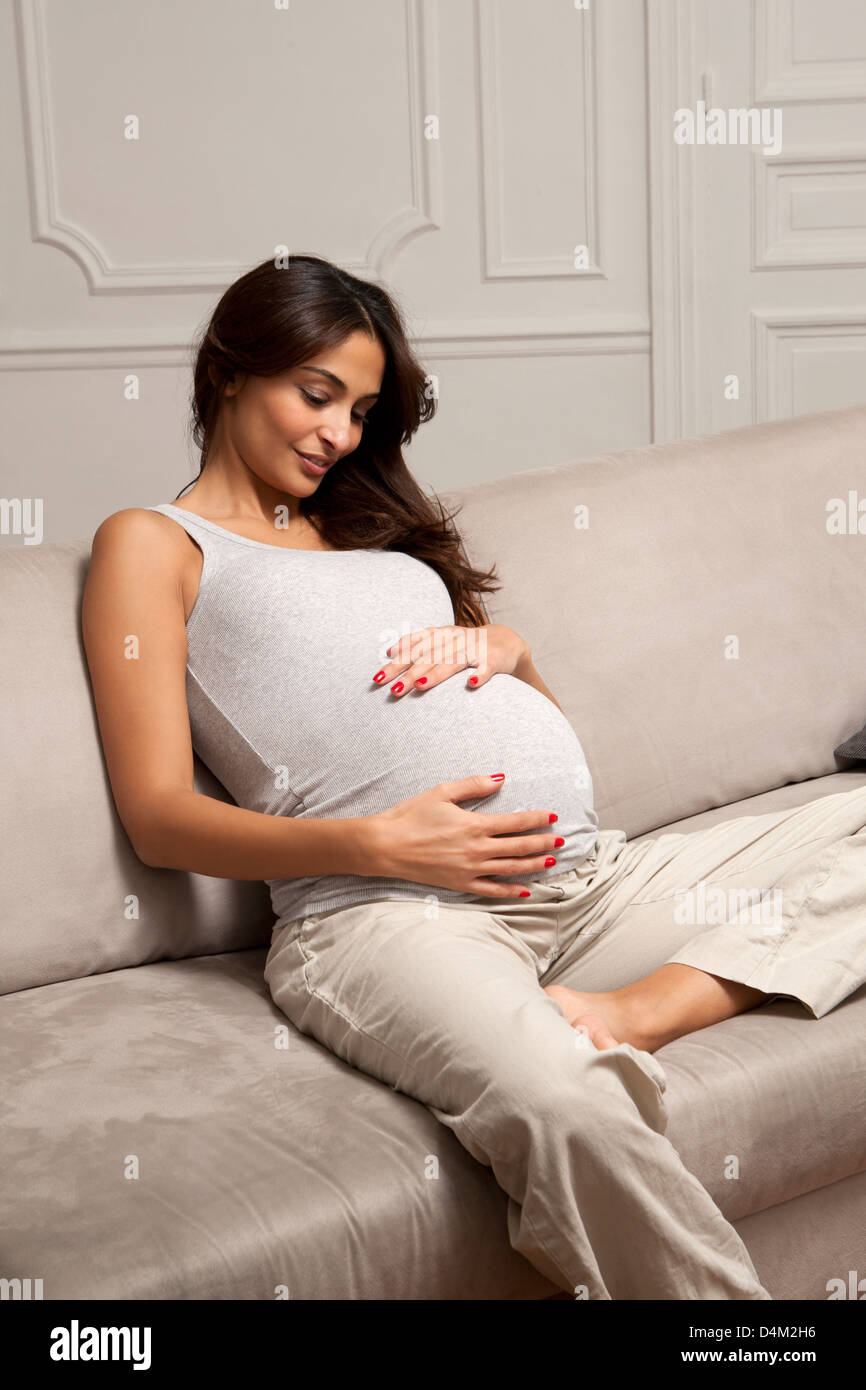 Pregnant woman holding belly on sofa Stock Photo Alamy