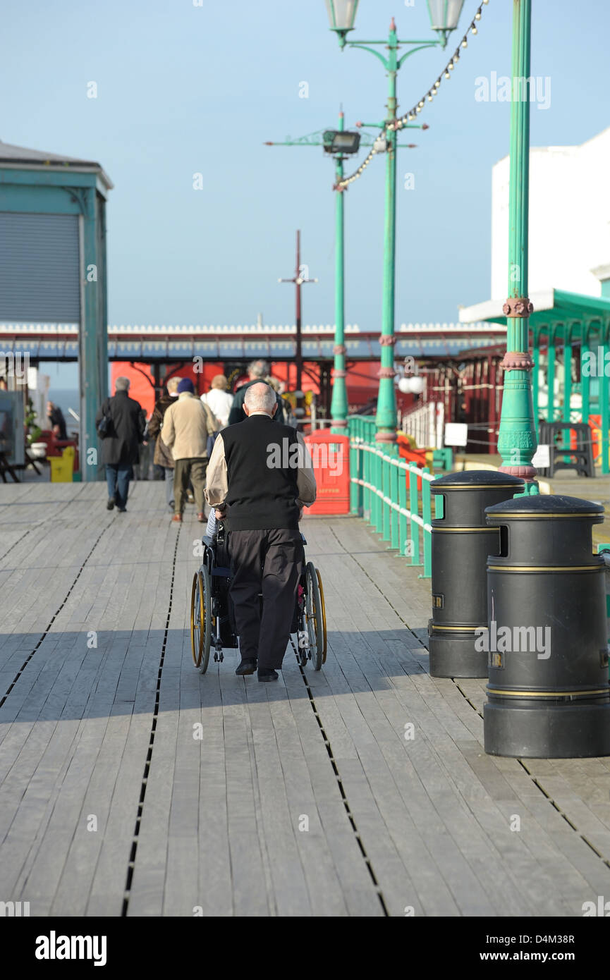 Disabled person being pushed down a holiday resort pier Stock Photo