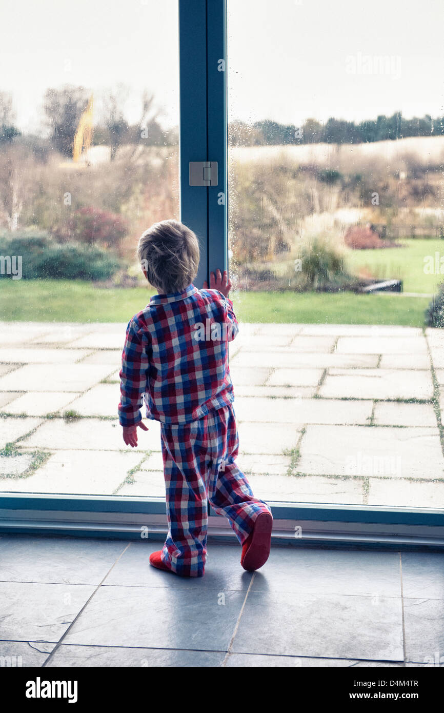 Boy in pajamas looking out window Stock Photo