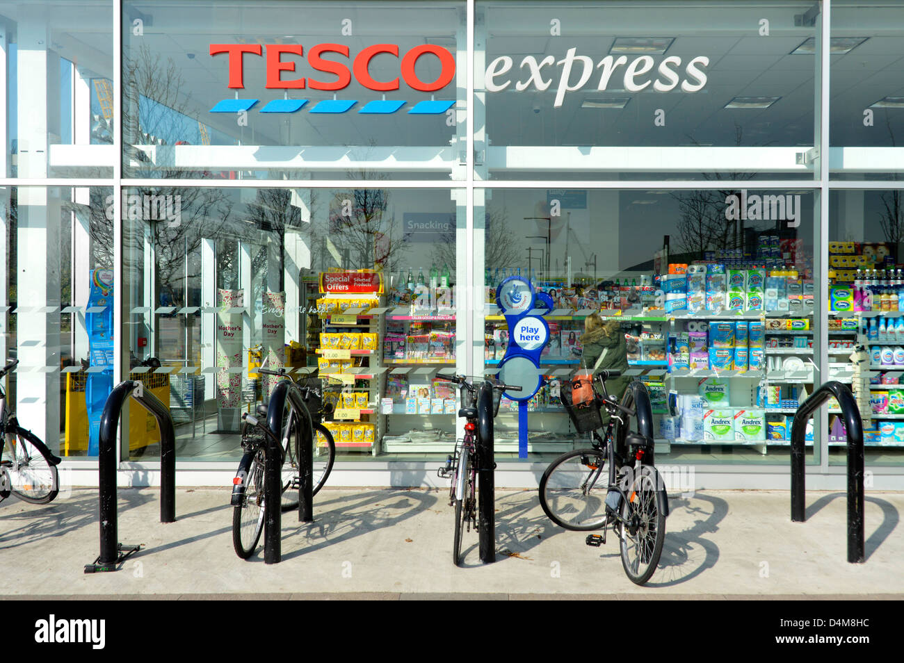 Bike racks outside convenience store window & view into tesco express grocery food drink supermarket retail business North Greenwich London England UK Stock Photo