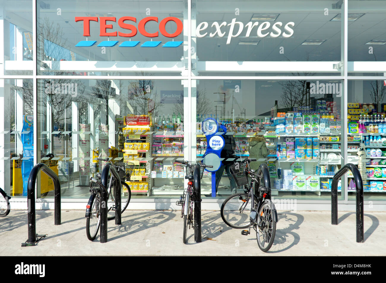 Bike racks outside convenience store window & view into tesco express grocery food drink supermarket retail business North Greenwich London England UK Stock Photo