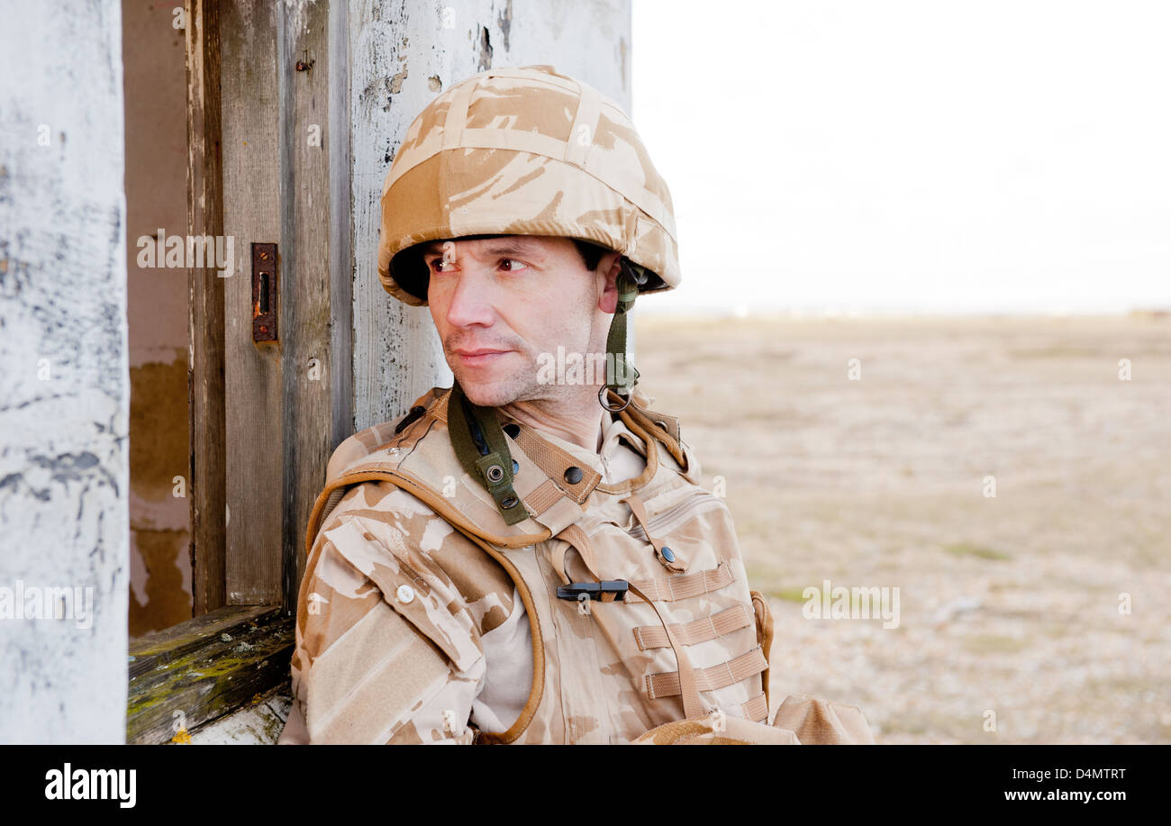 British soldier wearing desert camouflage uniform and looking through the window of a derelict building. Stock Photo