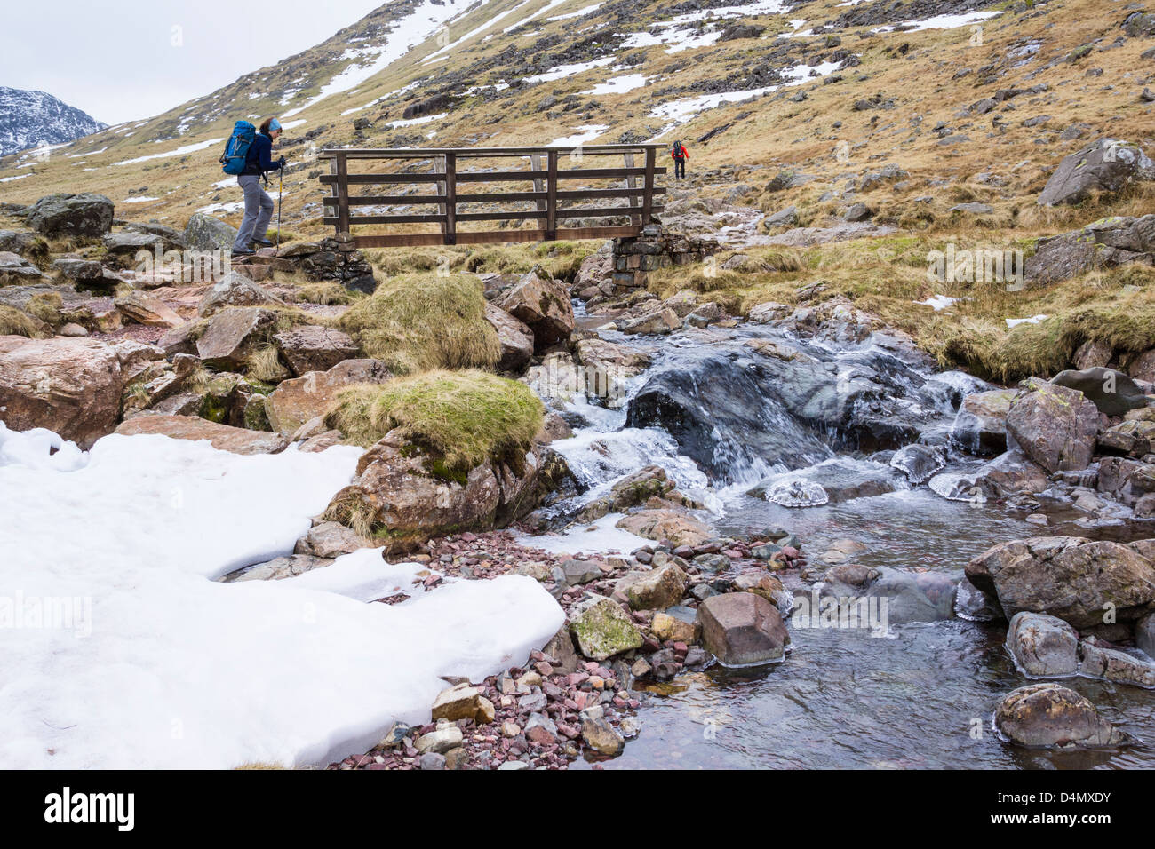A hiker crossing the stream at Styhead Gill in the Lake District Stock Photo