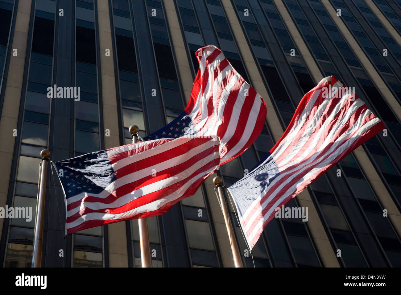 Three US stars and stripes flags flying in the wind in front of a skyscraper in New York, USA Stock Photo
