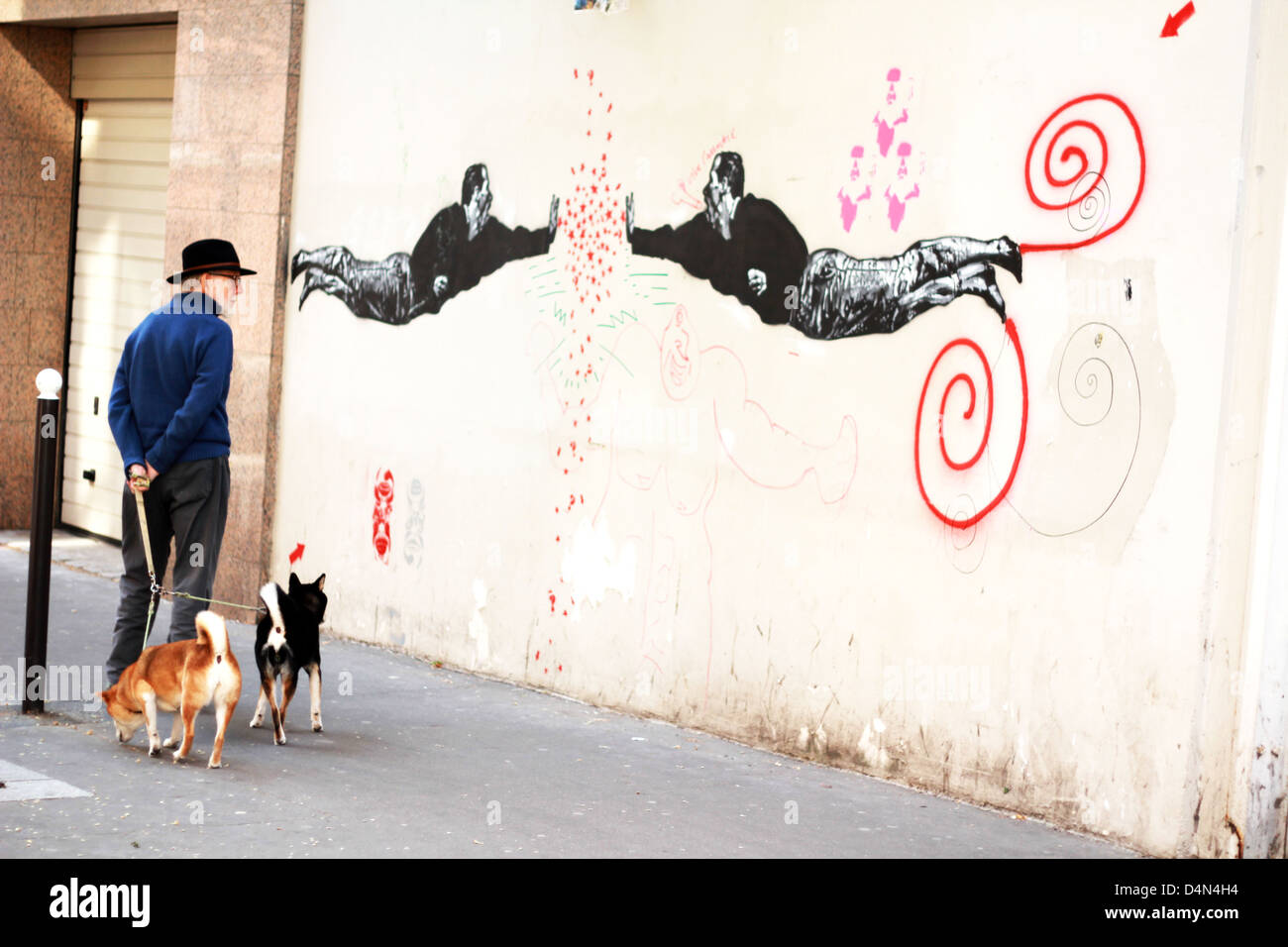 Senior man walking his two dogs stops to watch a wall graffiti, Paris, France Stock Photo
