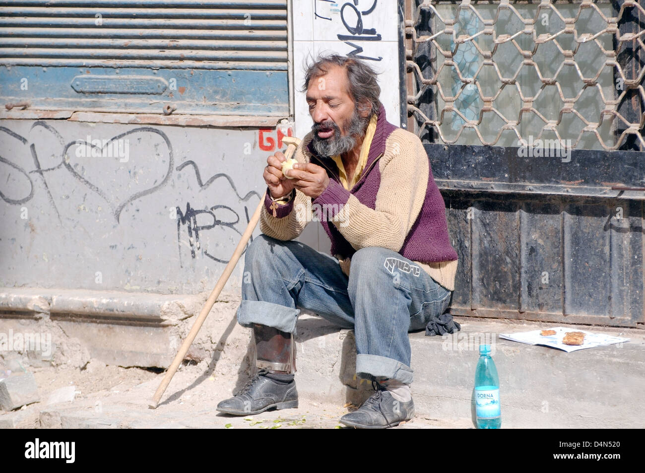 An elderly homeless man eating on the street, Bucharest, Romania