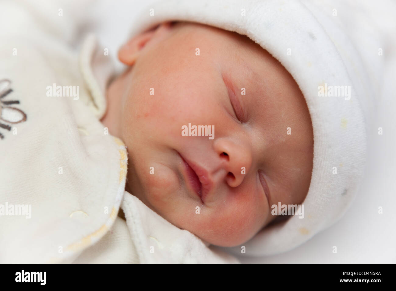 Newborn sleeping baby girl wrapped in a fleece bodysuit and hat. Taken at precisely 2 hours old. Focus on eye. Stock Photo