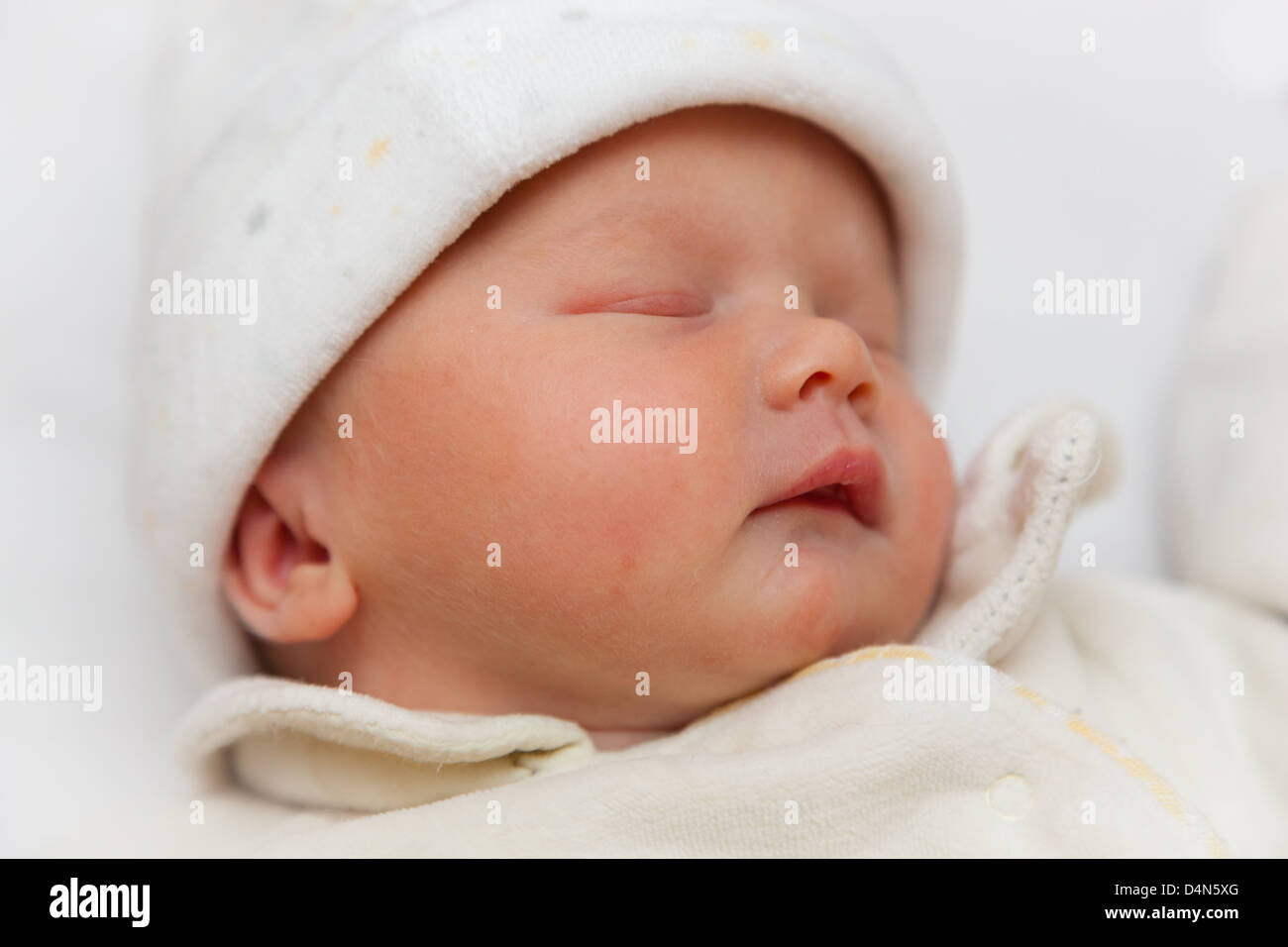 Beautiful newborn sleeping baby girl wrapped in a fleece bodysuit and hat. Taken at precisely 2 hours old. Focus on eye. Stock Photo