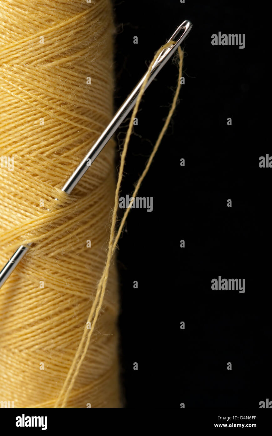 Close up of needle and yellow thread against black background Stock Photo
