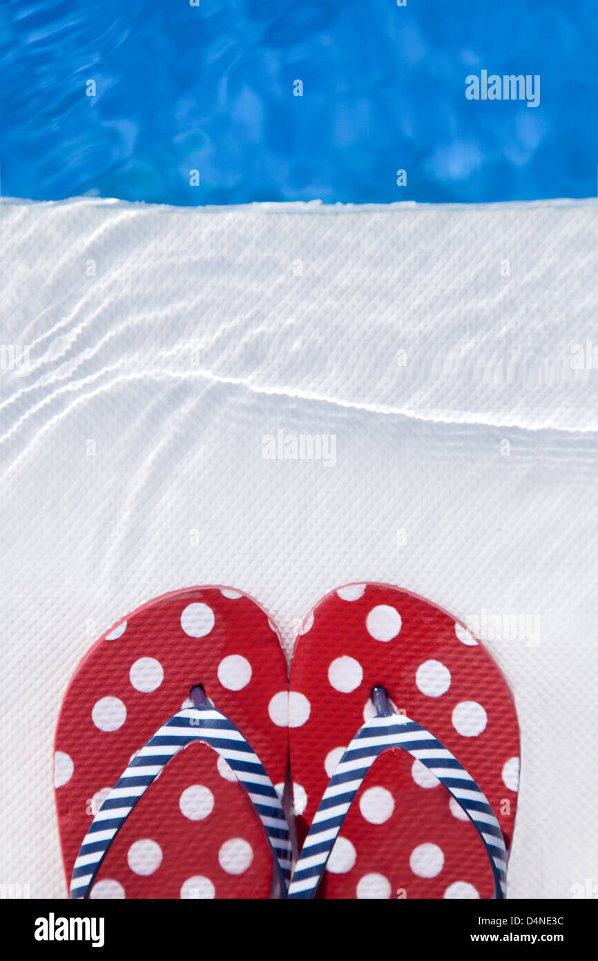 Pair of red flip-flop sandals with white spots by the swimming pool. Stock Photo