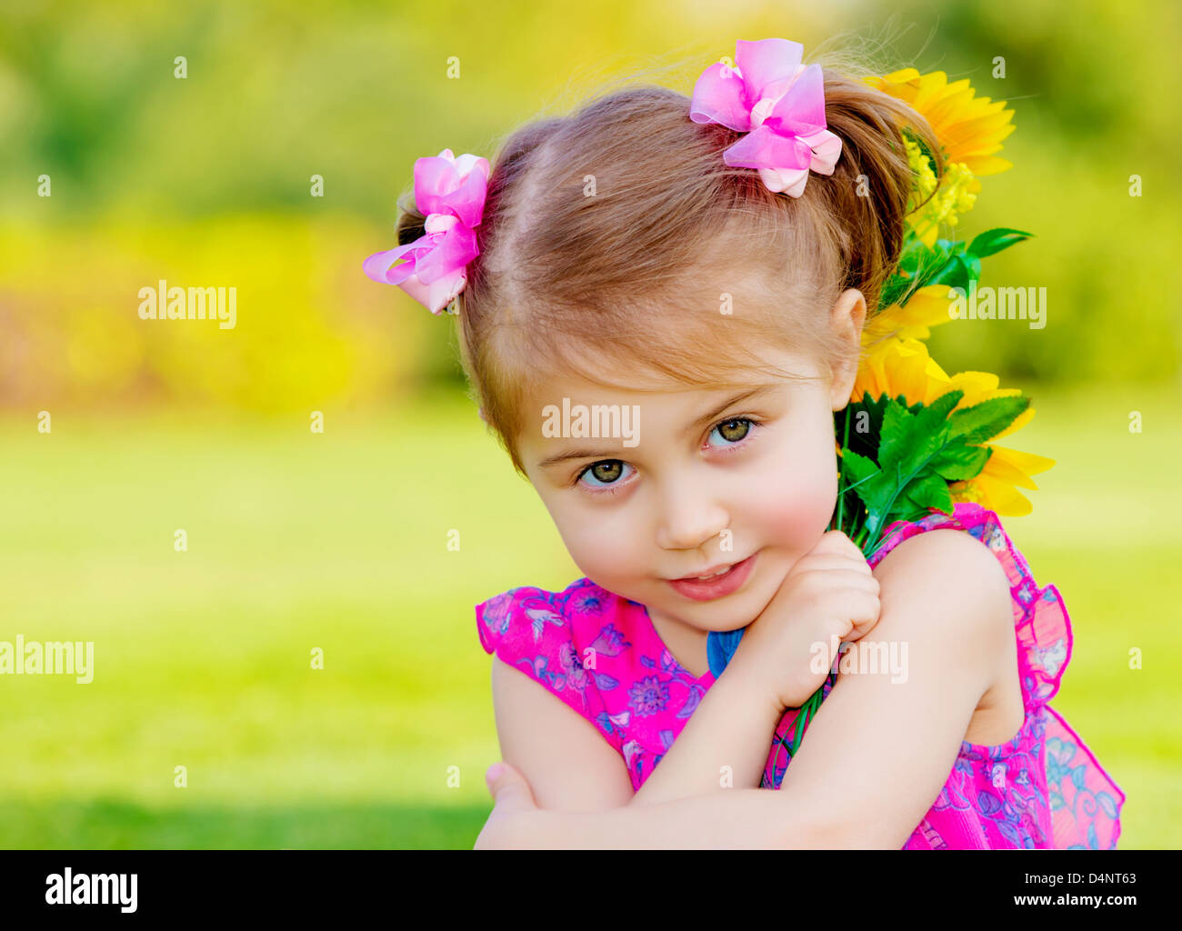 Happy baby girl playing outdoor, cute child holding fresh sunflower flowers, kid having fun in summer park Stock Photo