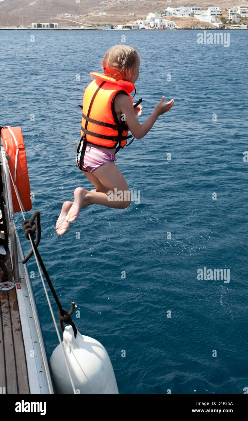 little girl in life jacket jumping to sea water from yacht deck Stock Photo