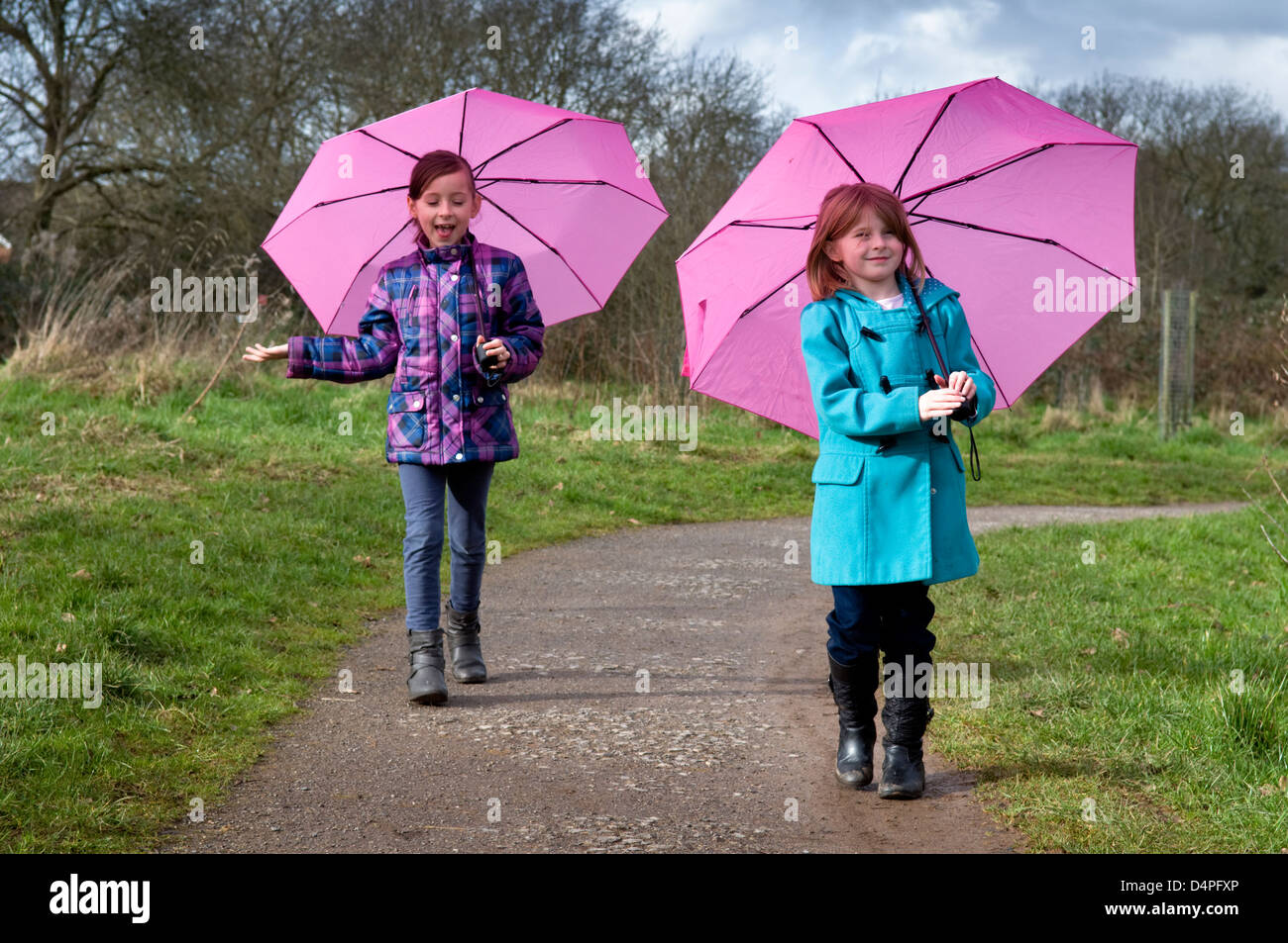 Two 8 year old Caucasian girls walking with pink umbrellas up Stock Photo