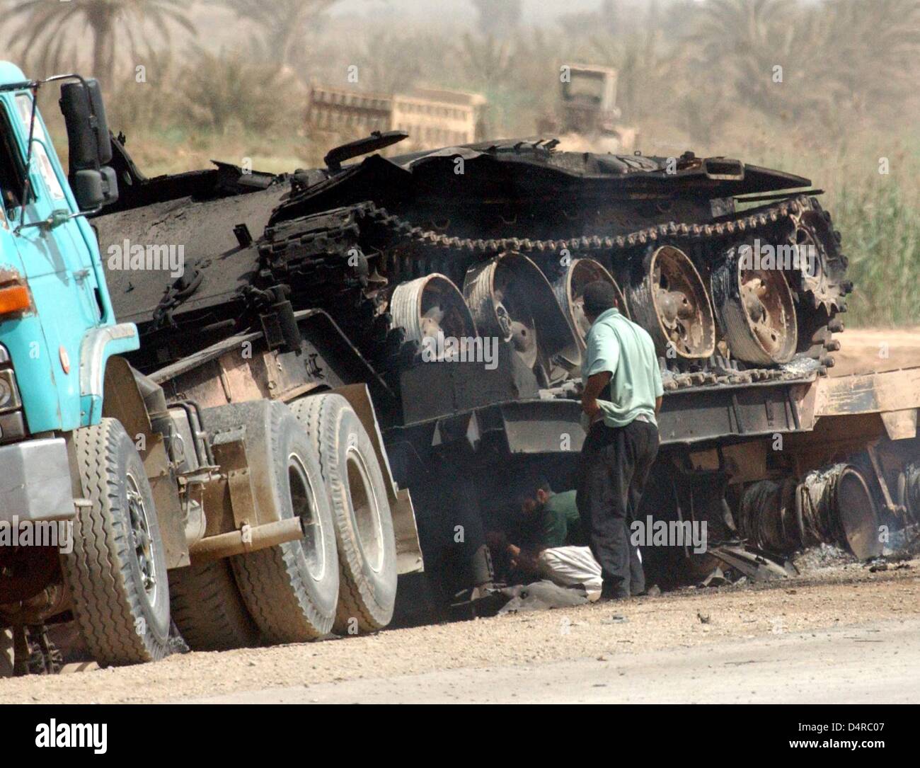 Iraqi civilians dismantle a destroyed Iraqi battle tank, on 4 April 2003, near Al Aziziyan, 40 km south of Baghdad. Stock Photo