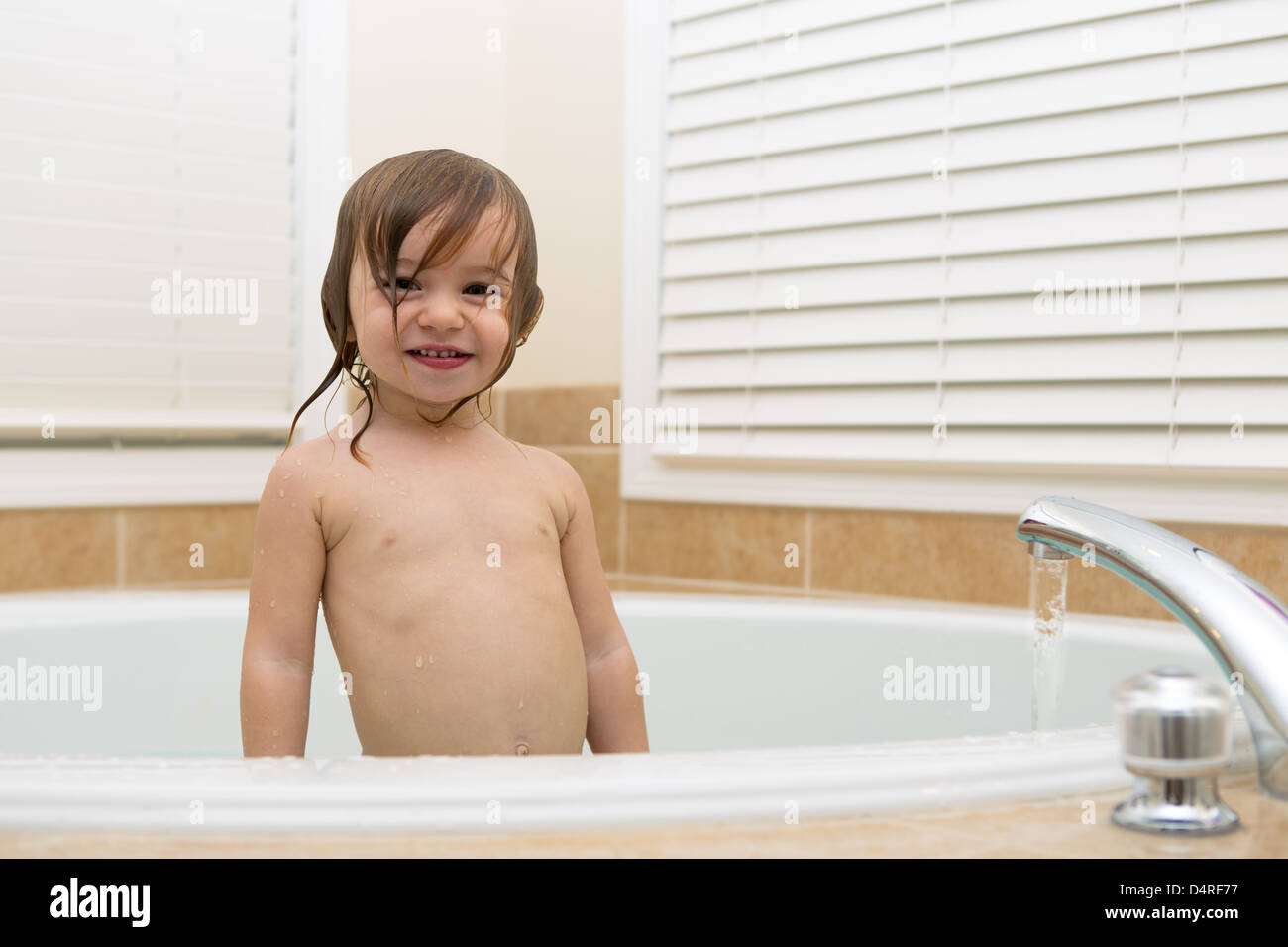 Toddler girl smiling trustfully from bath tub. Water coming from the