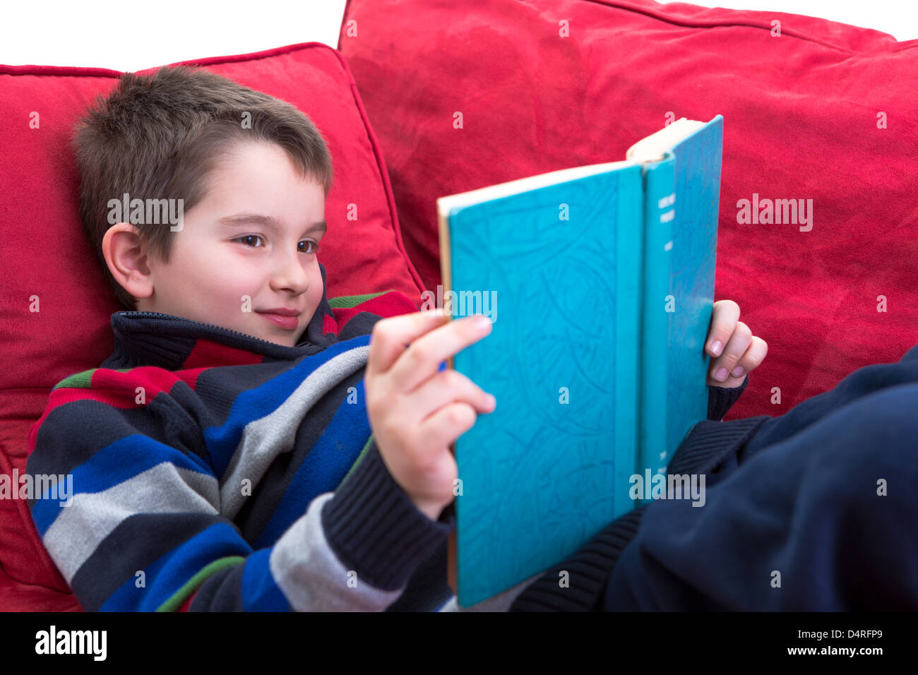Kid enjoy reading the novel on the comfortable red couch. Stock Photo