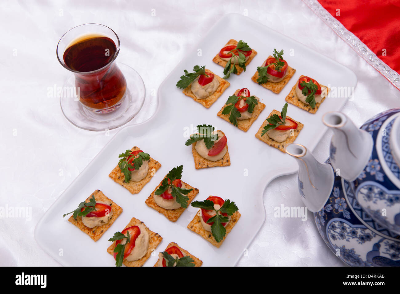 Crackers with hummus, red peppers and parsley in a white square plate served with hot tea . Stock Photo