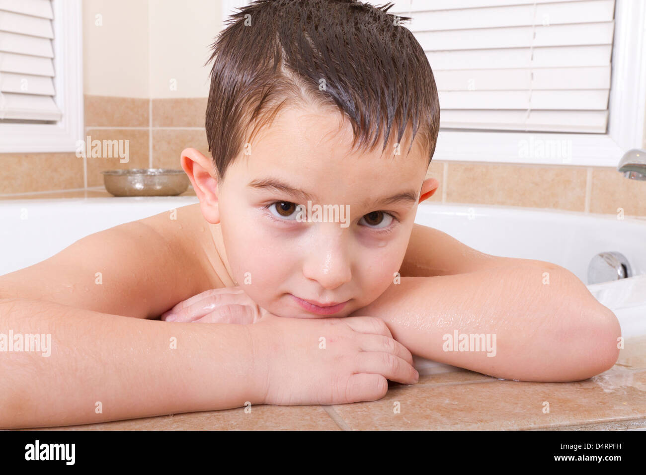 Seven years old kid looking at you ruminatively from a bath tub. Stock Photo