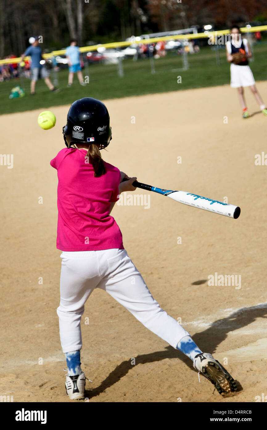 A young girl in a pink top plays softball,in readiness for playing