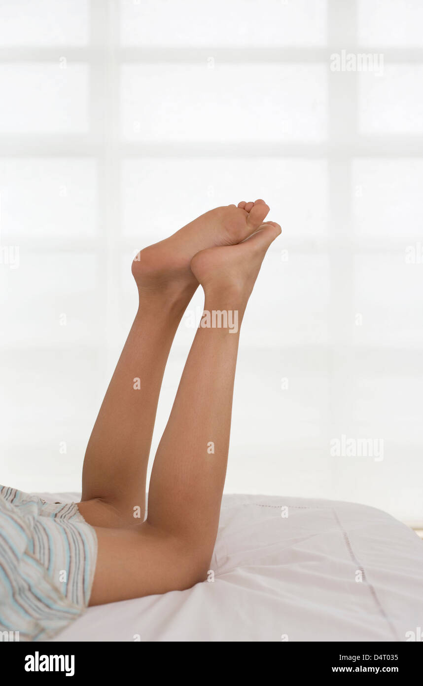 Raised Legs of Girl Lying on Bed Stock Photo