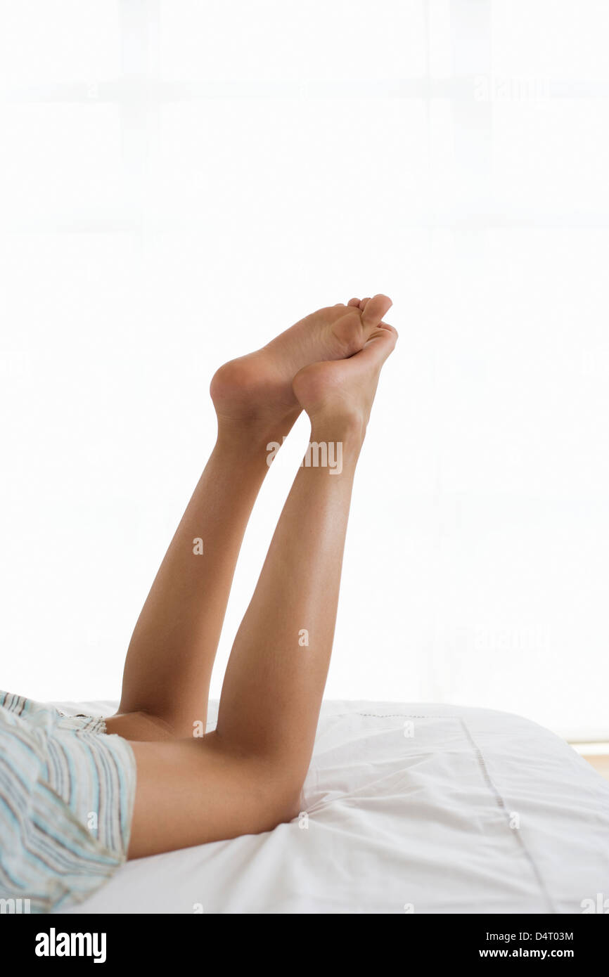 Raised Legs of Teenage Girl Lying on Bed Stock Photo