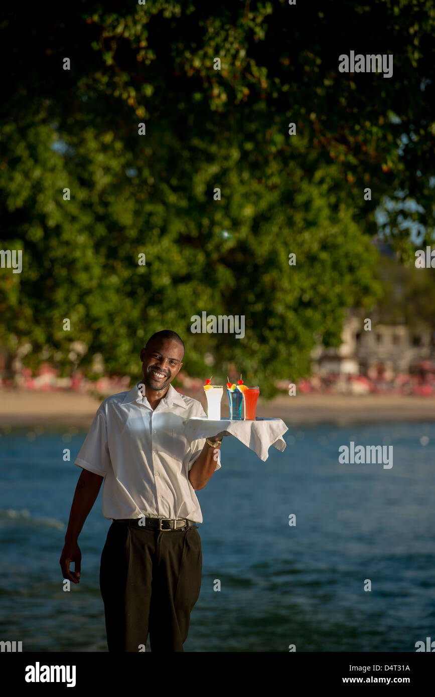 A waiter holding a tray of cocktail drinks on the west coast of Barbados, Holetown (Sandy Lane in background) Stock Photo