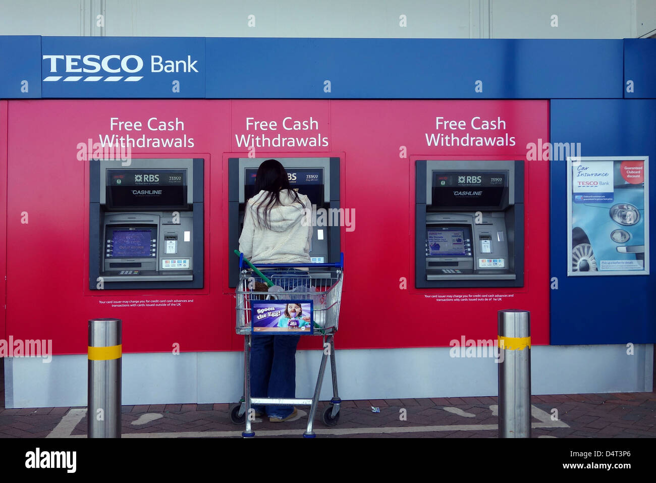 a young woman using a cash dispensing machine outside  a tesco supermarket Stock Photo