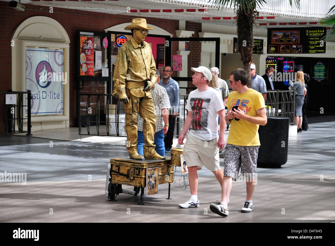Visitors walk by a living statue dressed as a cowboy and covered with gold paint Stock Photo
