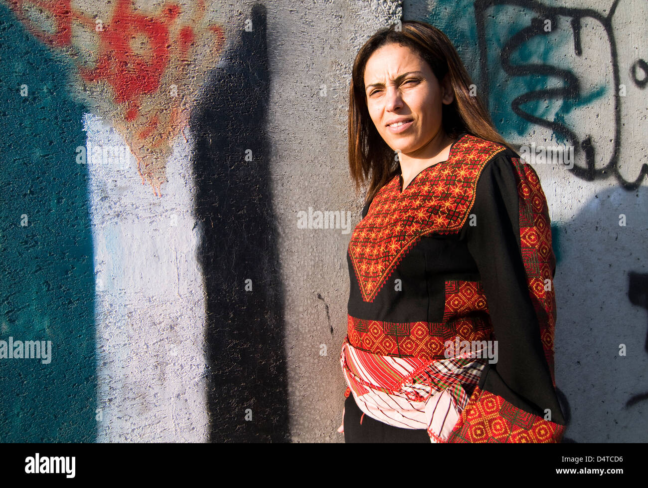 A proud Palestinian woman standing by the barrier built by the Israeli government. Art and graffiti decorate this concrete wall. Stock Photo