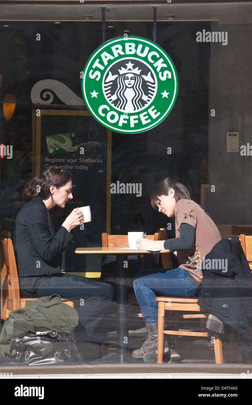 Two woman sat at the window inside a branch of Starbucks Coffee, on the Strand, central London, England, UK Stock Photo