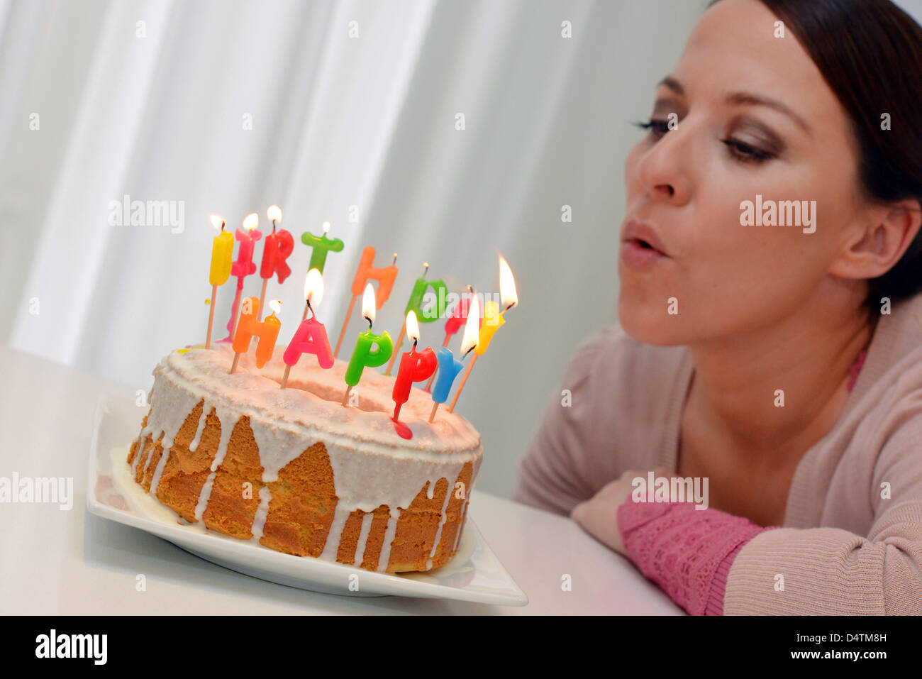 A young woman blows the candles of her birthday cake Stock Photo - Alamy