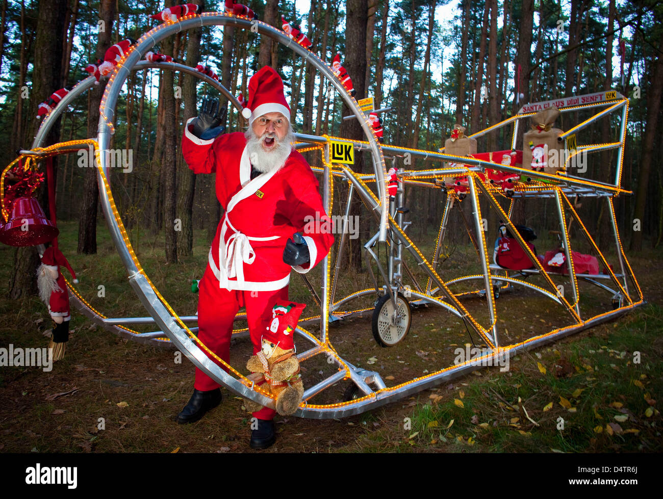 German action artist and bicycle designer Dieter 'Didi' Senft poses in a Santa Claus costume with his latest invention in Storkow, Germany, 24 November 2009. The new bike measures 7.30 metres length, 3.10 metres heigth, 2.00 metres width, weighs 800 kilograms and is illuminated with 3,000 light bulbs. As always, the invention is fully ridable. Senft has yet invented more than 200 u Stock Photo