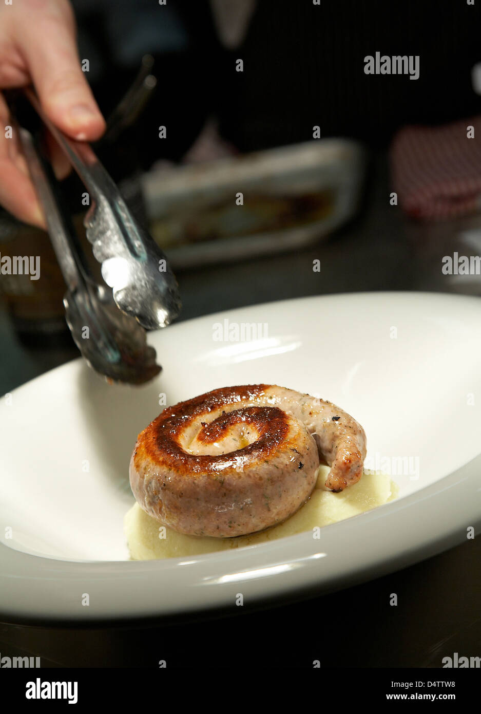 Chef placing a Cumberland sausage on a bed of mashed potato in a restaurant in the UK. Stock Photo