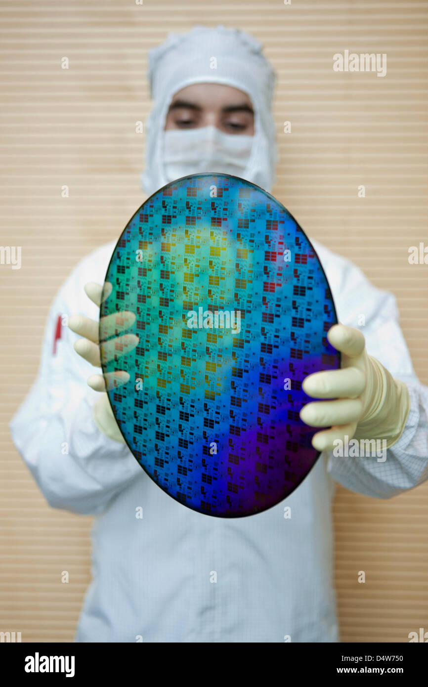An employee holds a 300mm large chip wafer in his hands, while the foundation of 'Fab 1 Annex' is layed at the site of chip manufacturer 'Globalfoundries' in Dresden, Germany, 15 September 2010. For 1,2 billion euro, Globalfoundries intends to expand its plant in Dresden. The founding stone was layed for a 10 000 sq.m large cleanroom on the area 'Fab 1'. Globalfoundries wishes to i Stock Photo