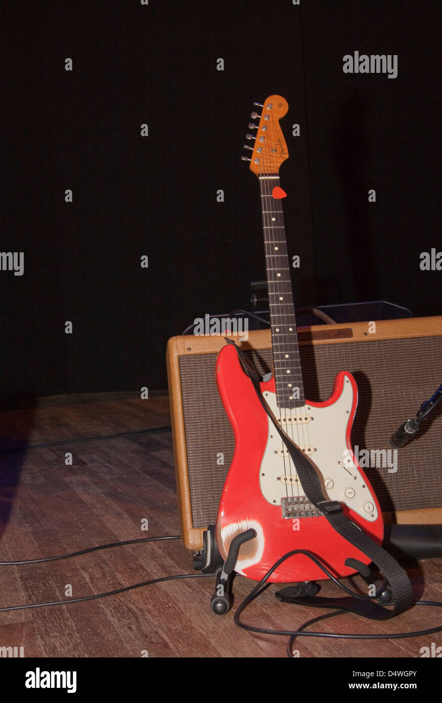 A bright red well used Fender Stratocaster electric guitar on a stand. Stock Photo